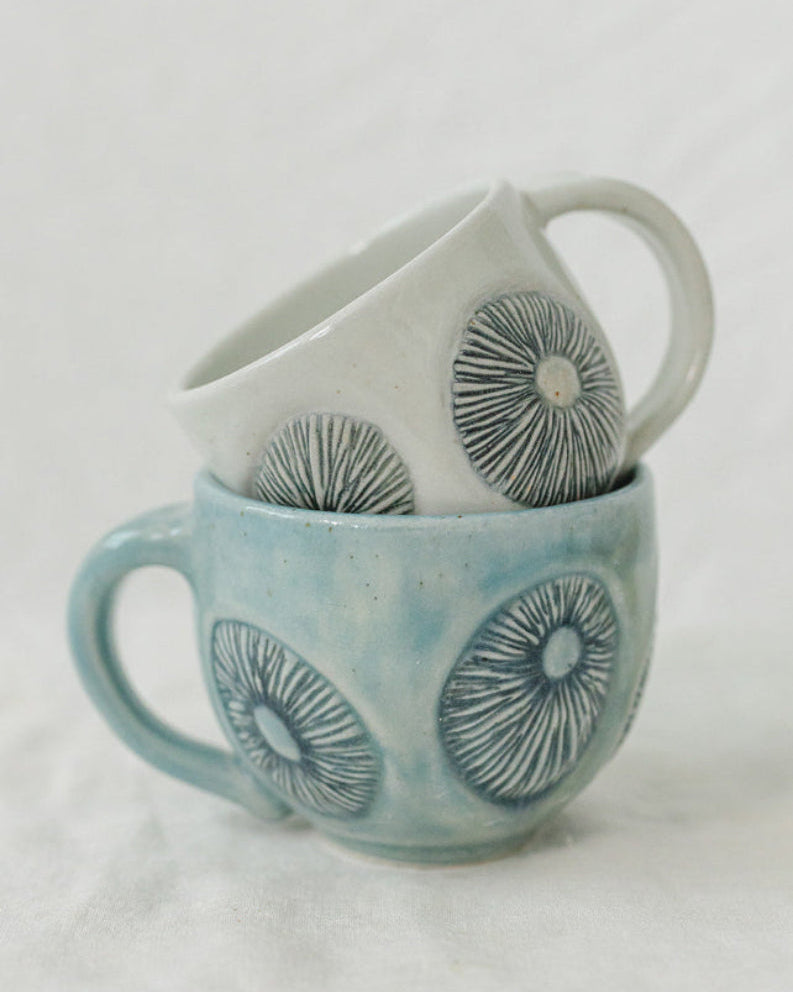 Two ceramic cups with barnacle patterns stacked on a light gray background