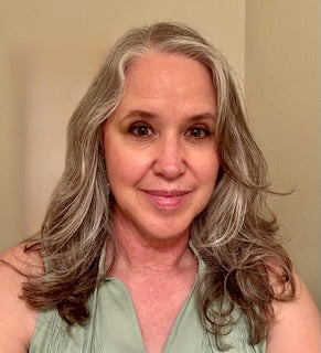 Woman with brown and gray hair wearing a green top against a beige background