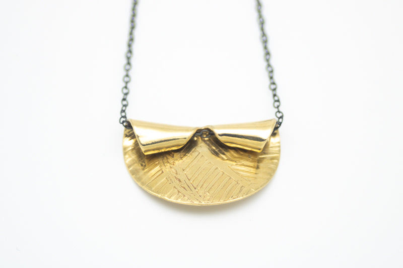 Handcrafted etched brass pendant necklace with a sculptural folded design on an oxidized sterling silver chain.