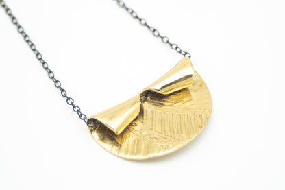 Handcrafted etched brass pendant necklace with a sculptural folded design on an oxidized sterling silver chain.