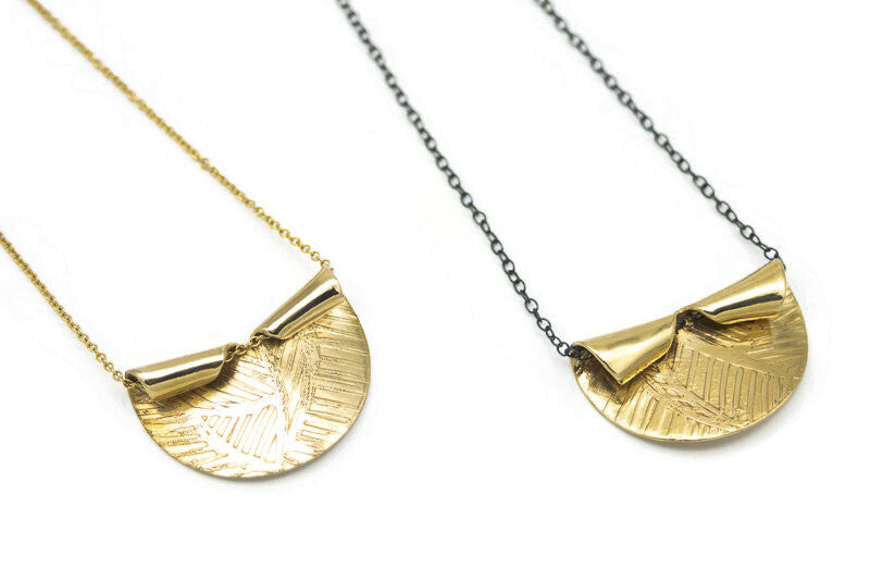 Handcrafted etched brass pendant necklace with a sculptural folded design on an oxidized sterling silver chain.